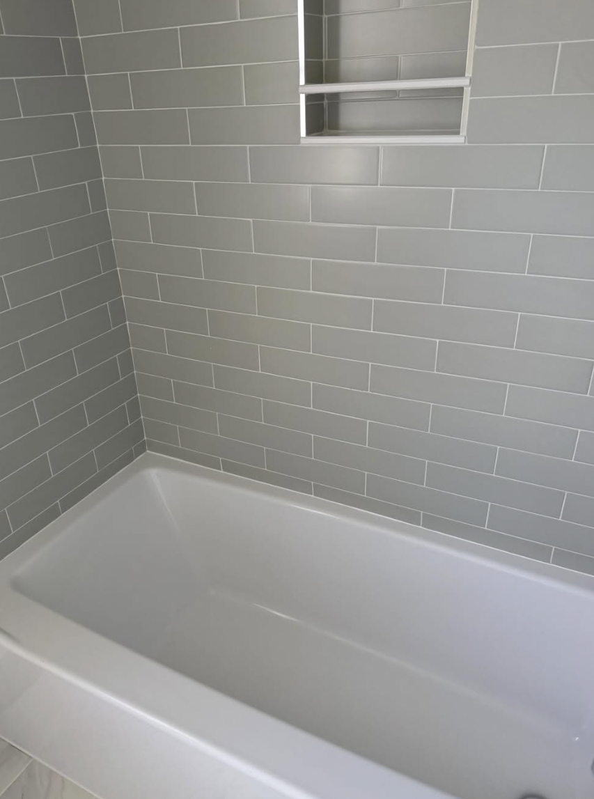 Grey subway tile shower surround and white bathtub scrubbed and streak-free
