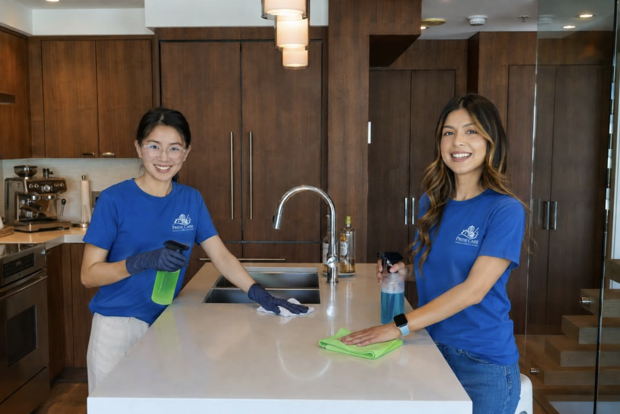 Two Pride Care Cleaning team members in branded blue shirts cleaning a modern kitchen island in Durham, NC